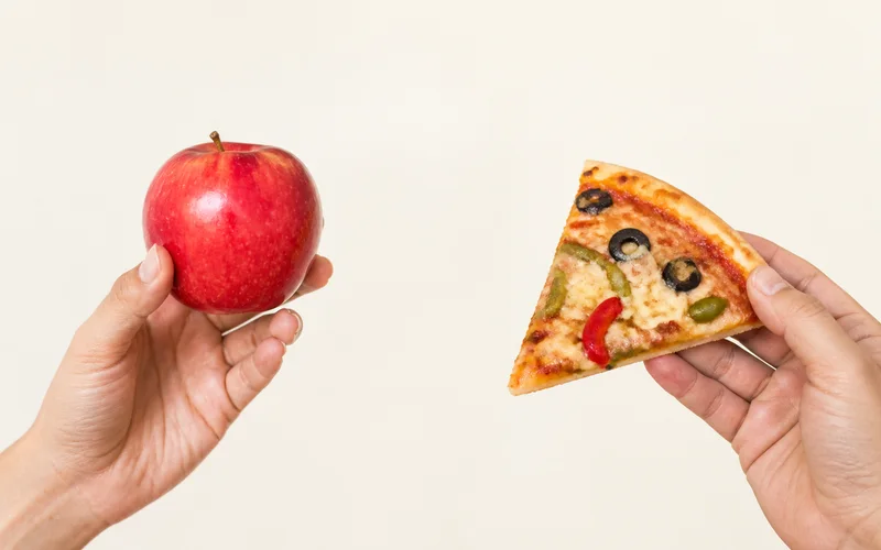An apple and a vegetable pizza slice held side by side